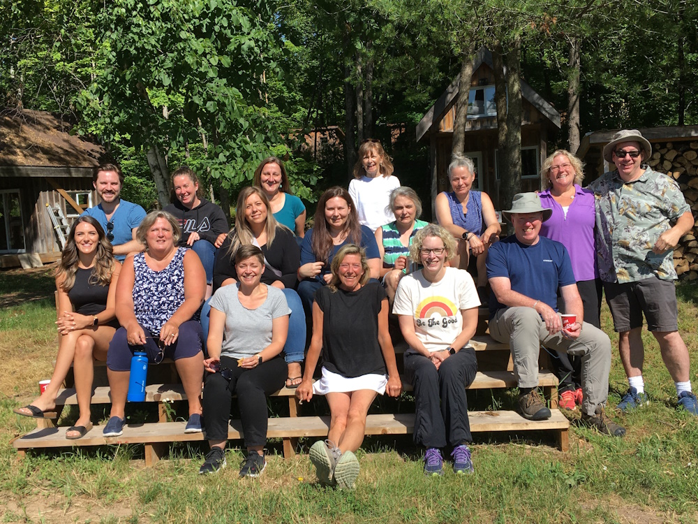 Hospice Peterborough staff sitting on wooden bench at rustic camp