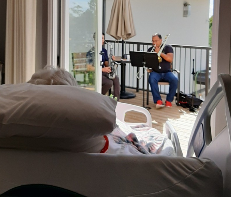 Men playing sax and trombone for Hospice patient in bed