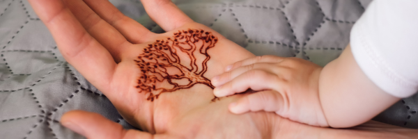 Henna tattoo of tree outline on a palm with a baby's hand resting on it